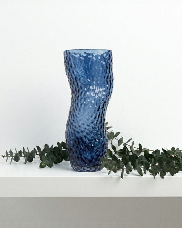 Blue textured vase on a light gray surface with a book titled 'Interior Living'.