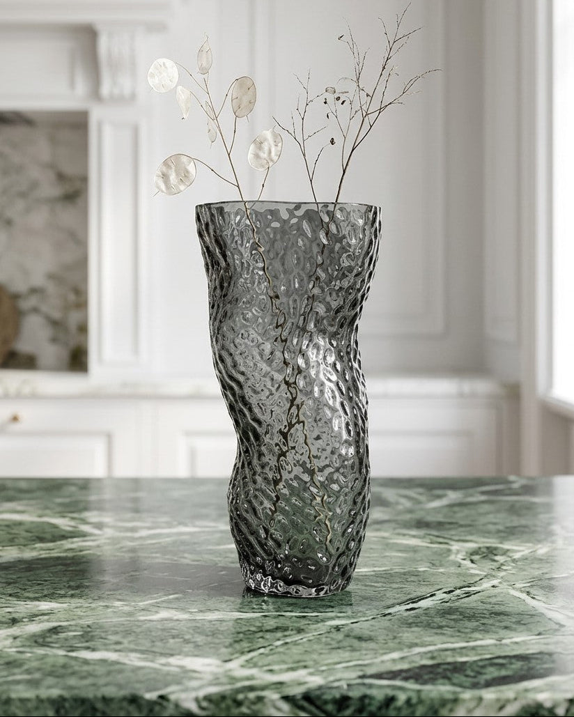 Textured gray vase with white flowers on a light surface with books in the background